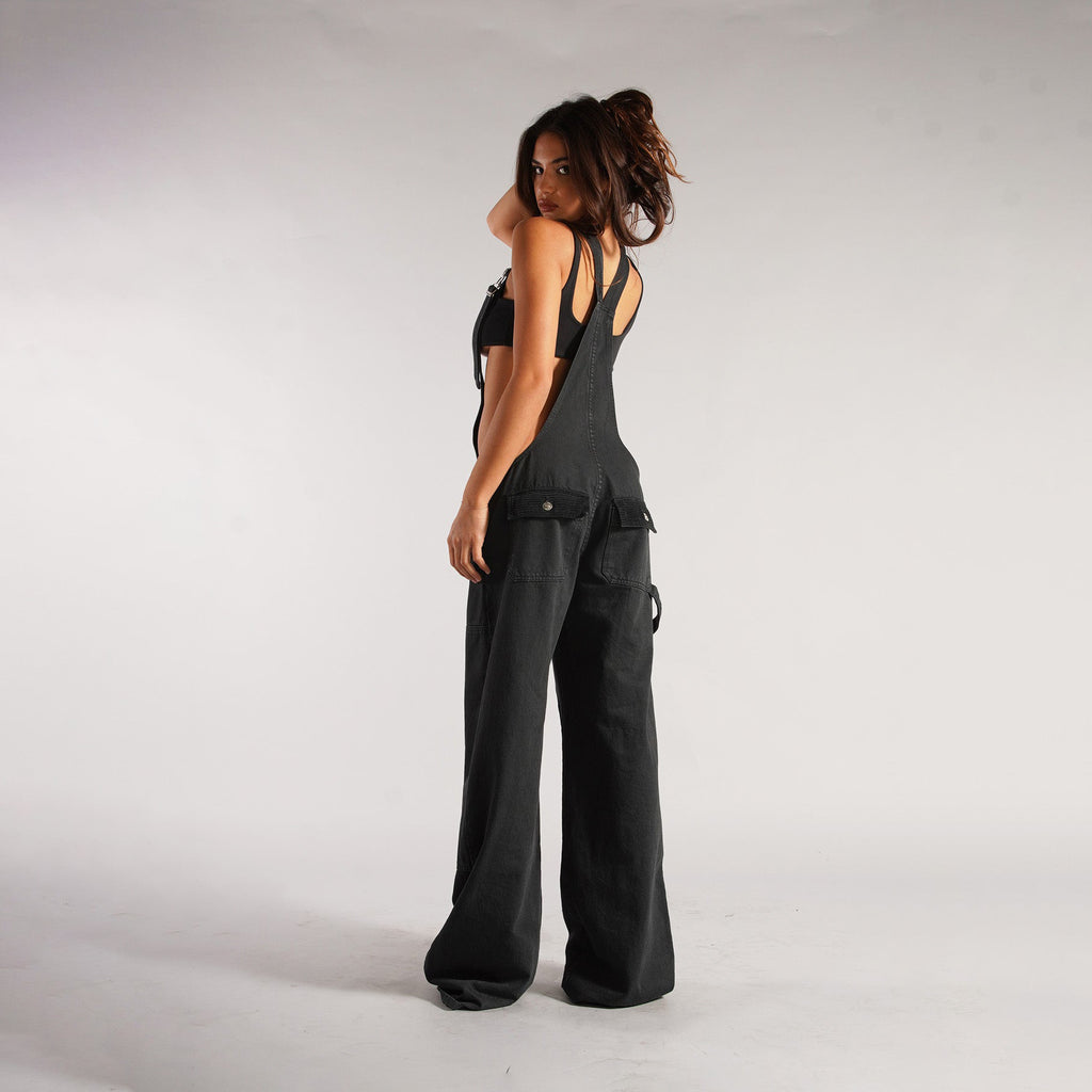 Black denim zipper overalls side view with suspender straps, wide legs, patch pockets