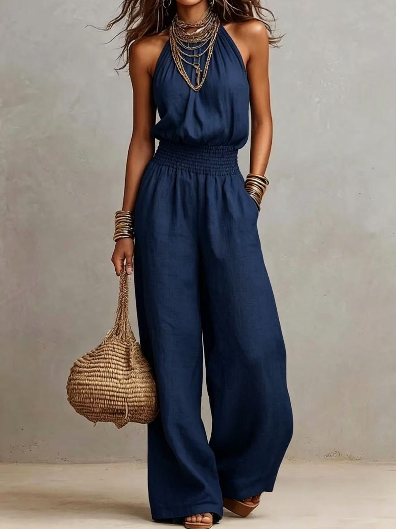 Navy blue sleeveless jumpsuit with halter neck, smocked waist, and wide legs