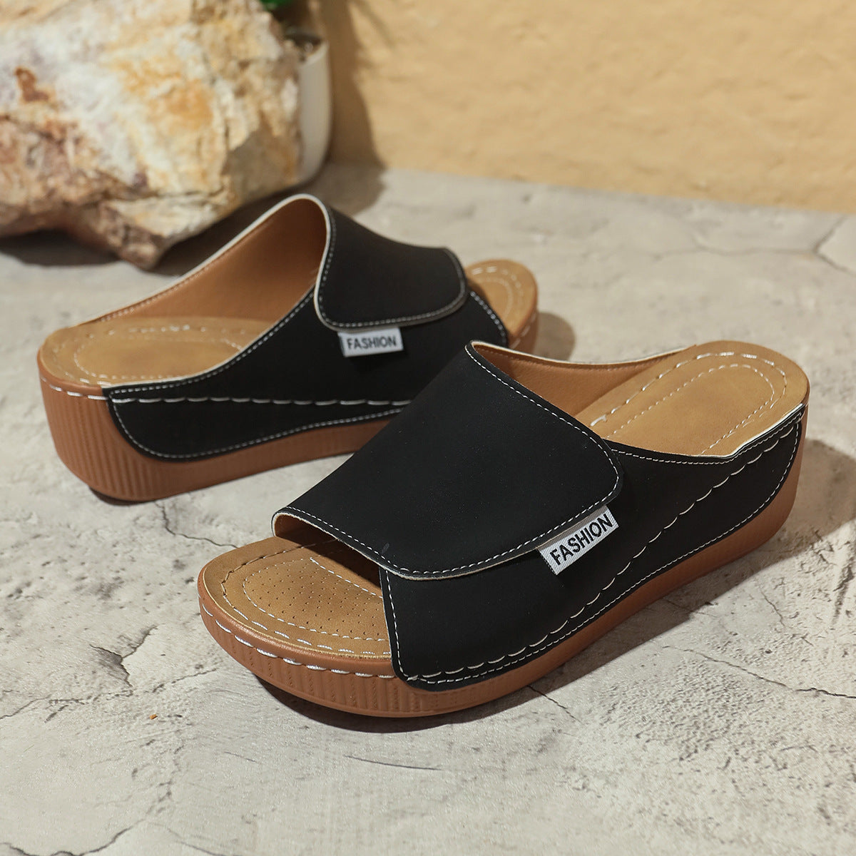 Black wedge slide sandals with open toe and contrast stitching on tan footbed