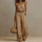 Light brown sleeveless jumpsuit with halter neck, smocked waist, and wide legs