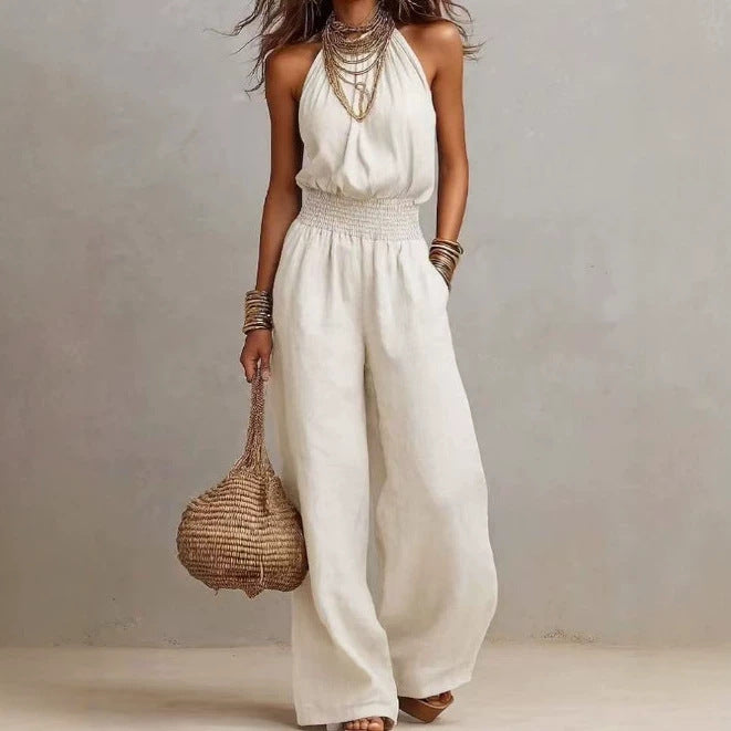 White sleeveless jumpsuit with halter neck, smocked waist, and wide legs